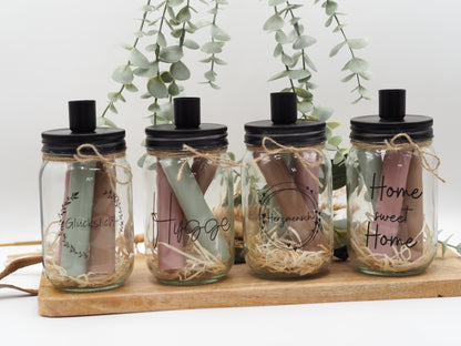 Beispielfoto von vier Stabkerzengläsern mit den Aufdrucken „Home Sweet Home“, „Glückslicht“, „Herzkranz/Herzmensch“ und Hygge.
